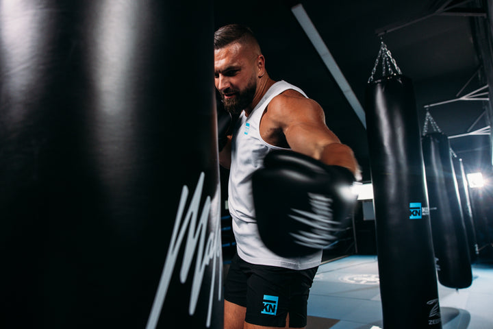 Kosso slaat een bokszak terwijl hij Malelions x KN sportkleding draagt in de sportschool.